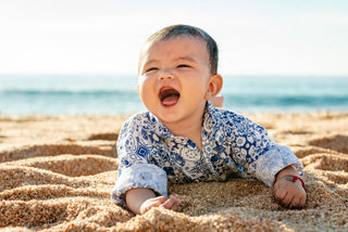 Baby laughing while lying on the sand at Fiesta Americana Los Cabos, ocean in the background